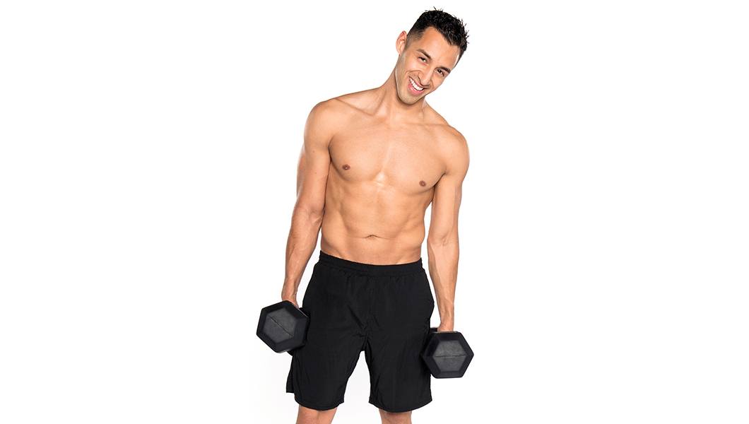 Shirtless Barry's Bootcamp instructor Andrew Nunez smiling while holding dumbbells by side on white background
