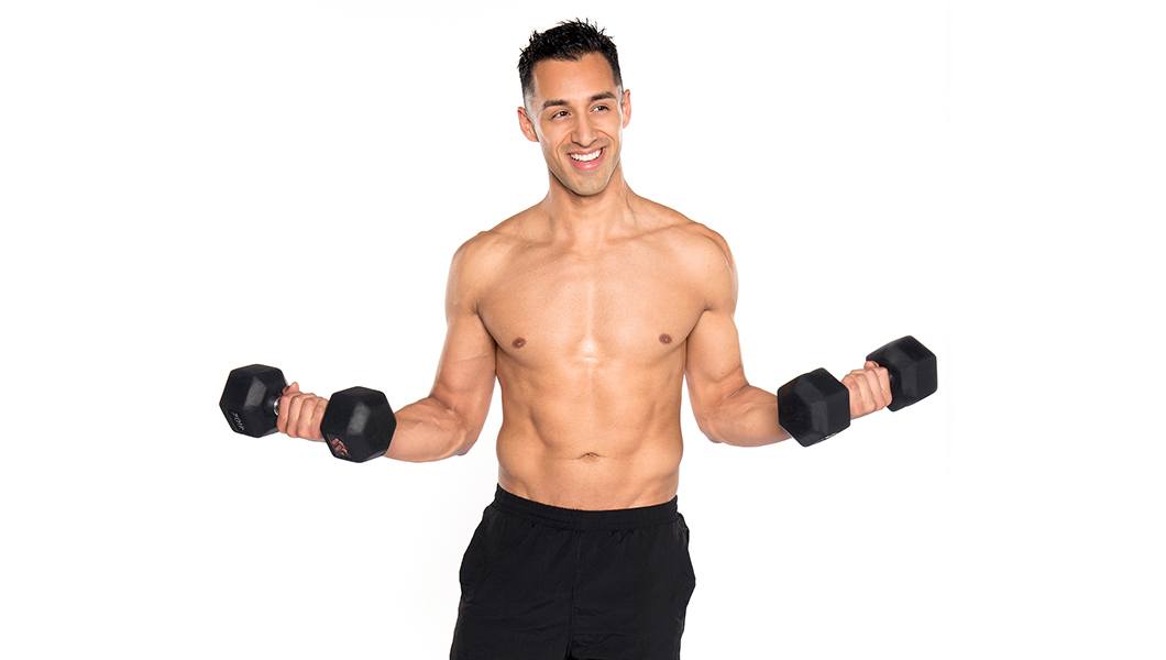 Shirtless Barry's Bootcamp instructor Andrew Nunez smiling while doing bicep curls with dumbbells on white background