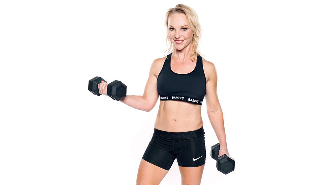 Barry's Instructor Brooke Sheely wearing black sports bra posing with dumbbells
