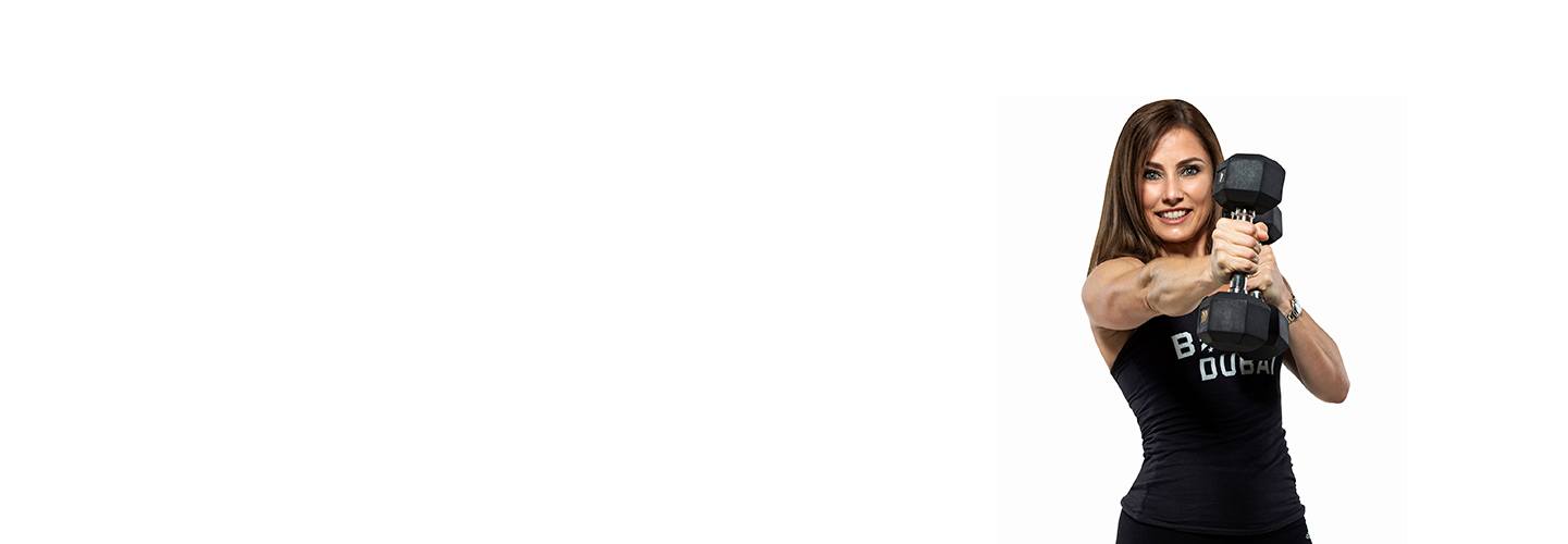 Instructor Charlotte in black Barry's Bootcamp tank top smiling while doing cross punch with dumbbells on white background