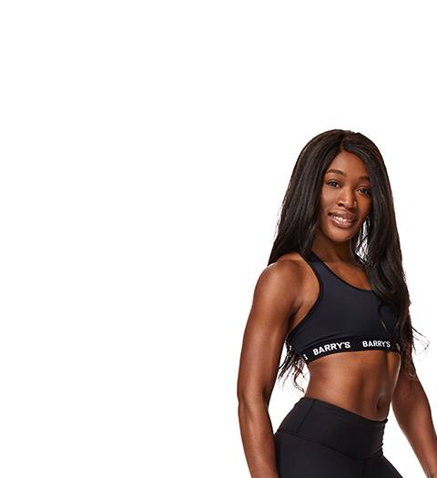 Barry’s instructor wearing a black top standing confidently smiling against a white background