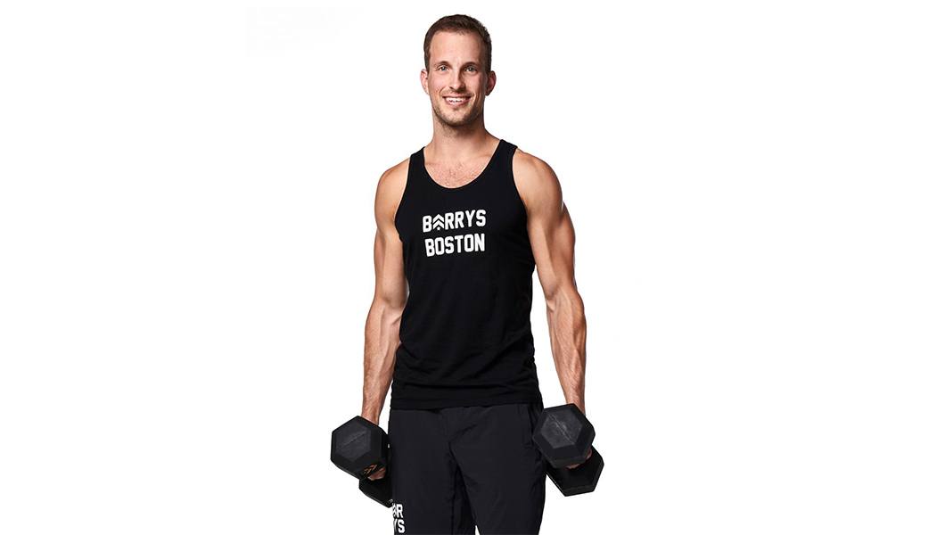 Instructor Greg Ux in black Barry's tank holding dumbbells at their side