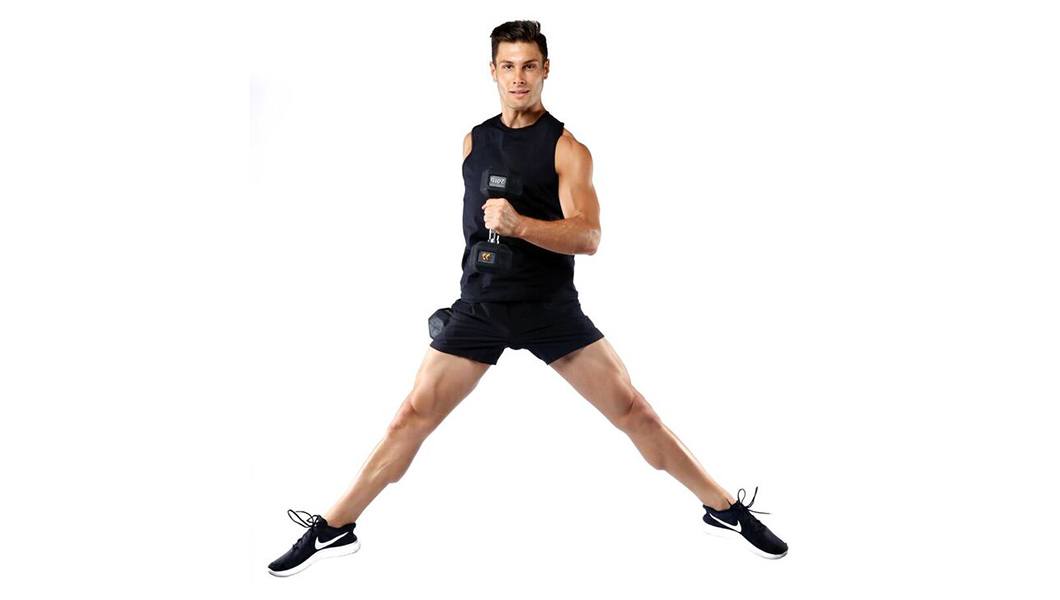 Barry's Bootcamp instructor Joe Nicastro in black tank top smiling while jumping with dumbbell in hand on white background