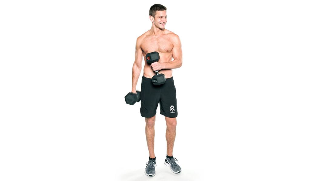 Shirtless Barry's Bootcamp instructor Jordan Gluck holding dumbbells and smiling on white background