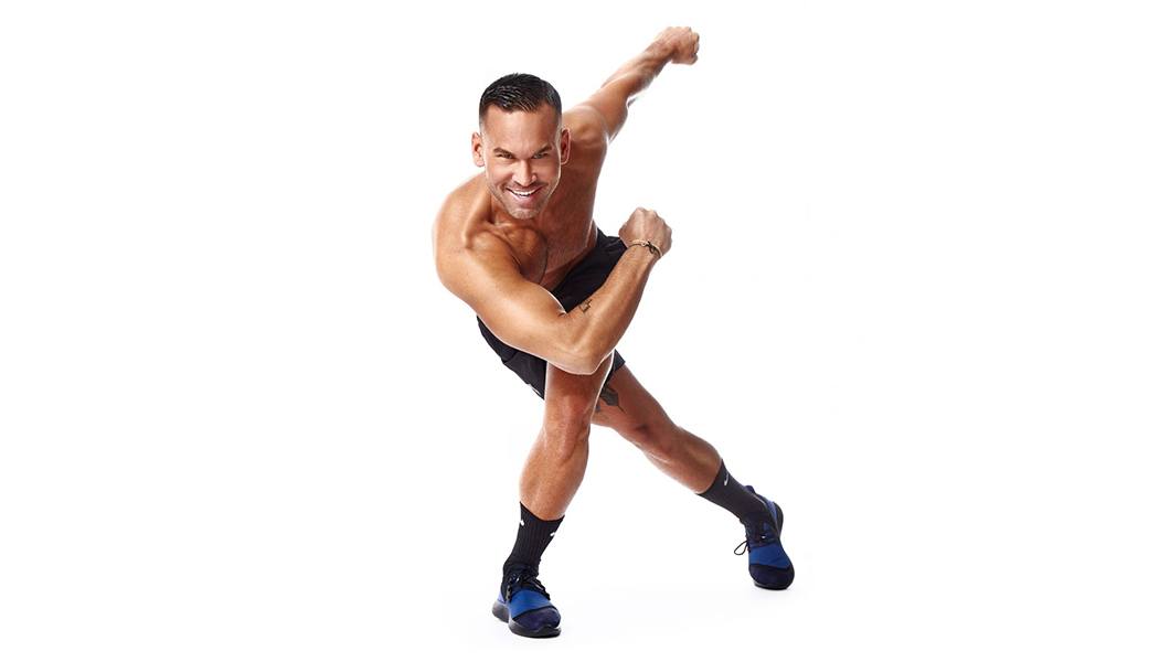 Shirtless Barry's Bootcamp instructor Keoni Hudoba doing side skier exercise on white background