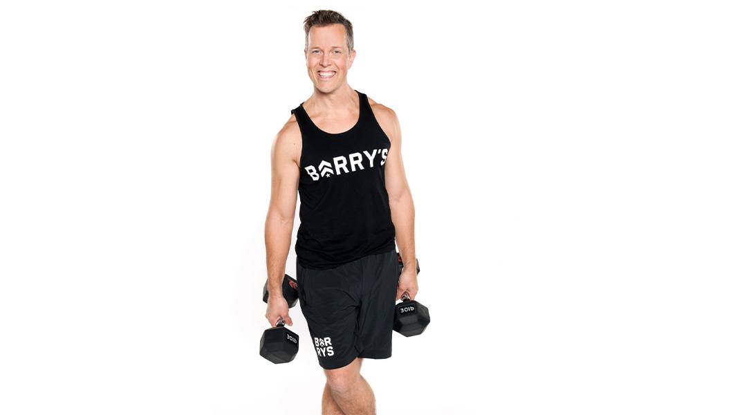 Barry's Instructor Martin George wearing black tank posing with dumbbells