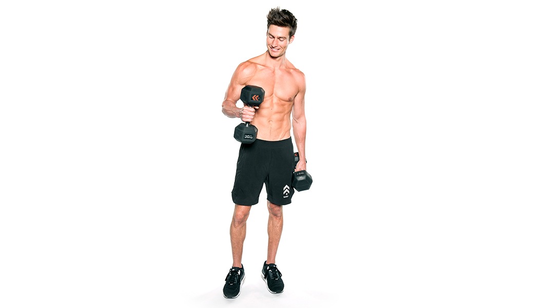Shirtless Barry's Bootcamp instructor Matt W doing cross bicep curl with dumbbells while smiling on white background