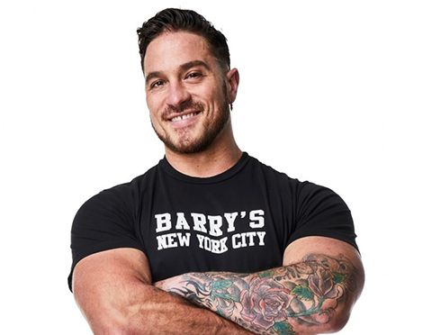 Barry’s instructor wearing a black top standing confidently smiling against a white background