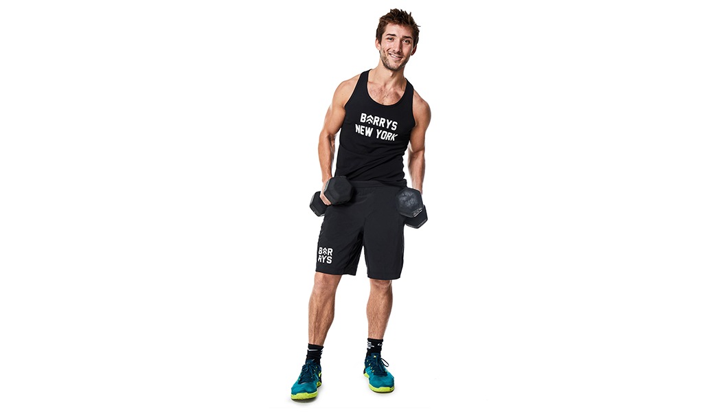 Barry's Bootcamp instructor Taylor Walsh holding dumbbells at his side.