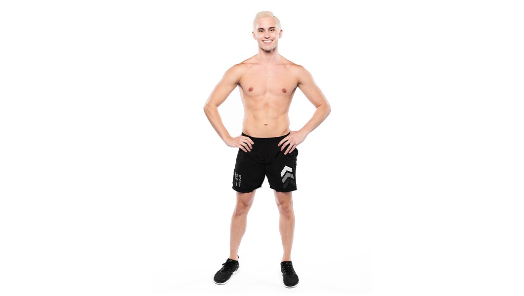 Barry’s instructor shirtless standing confidently with hands on hips smiling against a white background