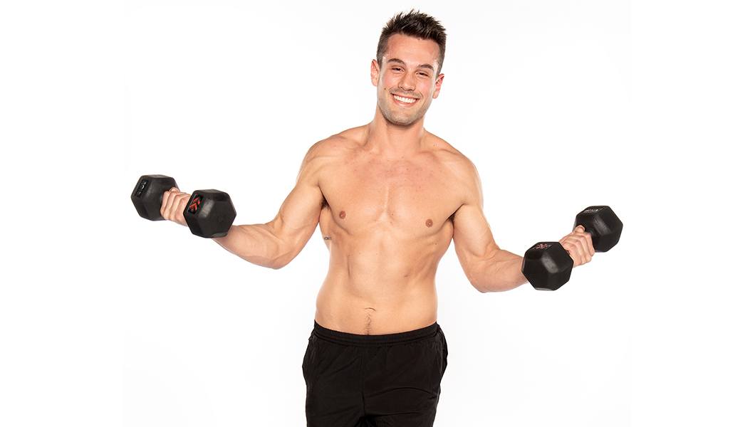 Barry's Bootcamp instructor Nick Tipple shirtless while holding dumbbells out to his sides against a white background.