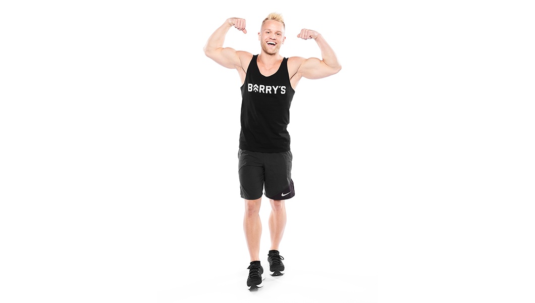 Barry’s instructor wearing a black tank top flexing standing confidently smiling against a white background