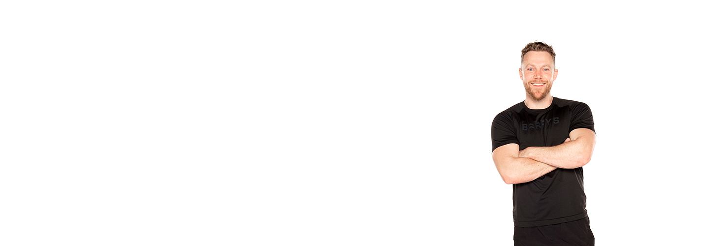 Barry's Bootcamp instructor Tommy Killen smiling in a black t-shirt with arms crossed against a white background.