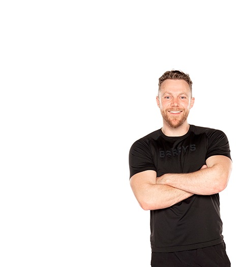 Barry's Bootcamp instructor Tommy Killen smiling in a black t-shirt with arms crossed against a white background.