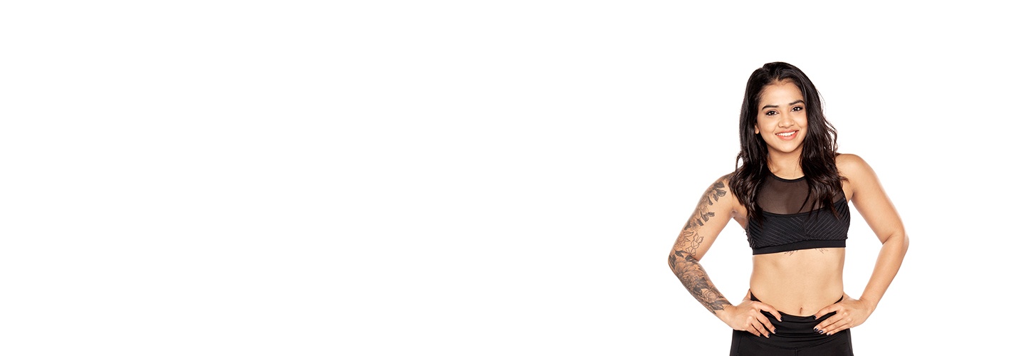 Barry's Bootcamp instructor Trishala Poulose wearing a black sports bra with her hands on her hips against a white background.