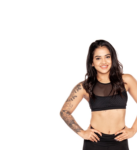 Barry's Bootcamp instructor Trishala Poulose wearing a black sports bra with her hands on her hips against a white background.