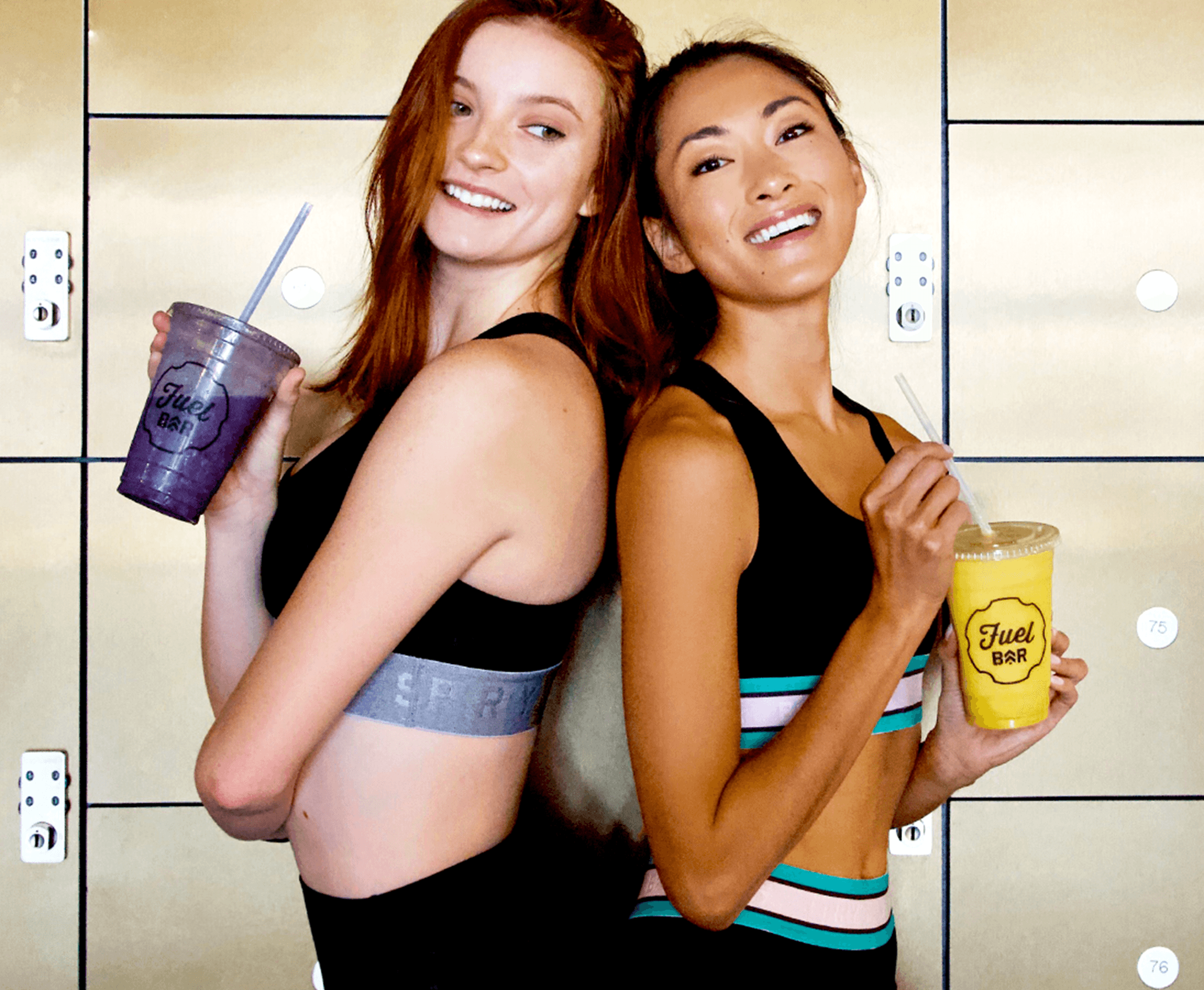 Two women wearing activewear back to back smiling with purple and yellow Fuel Bar drinks