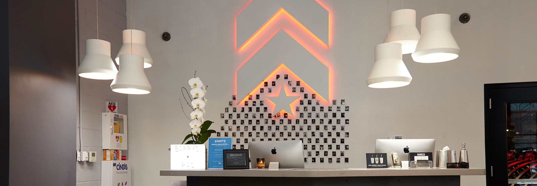 White Barry's Bootcamp upward arrows and star logo with red backlighting on wall behind reception desk at Park Ave South studio location