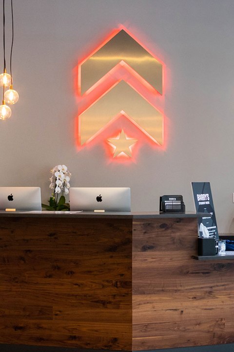 Gold Barry's Bootcamp upward arrows and star logo with red backlighting on wall behind reception desk at Back Bay studio location