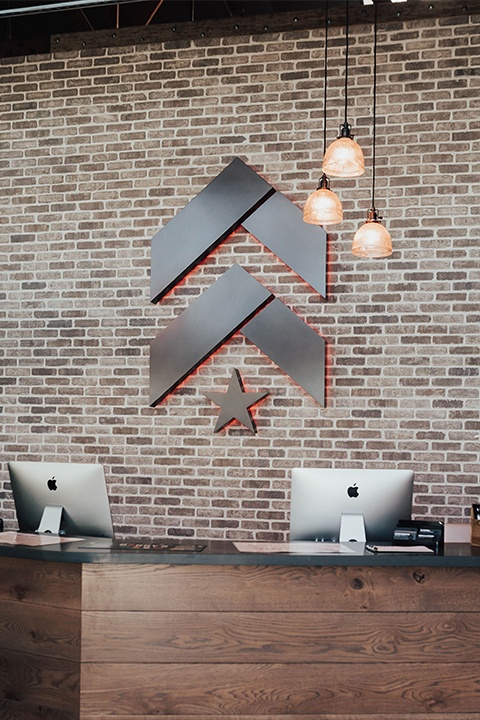 Slate Barry's Bootcamp upward arrows and star logo on grey brick wall in Burlingame studio reception area