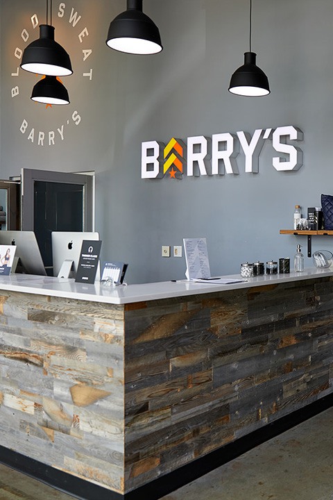 Barry's Bootcamp white sign and yellow and orange logo on wall behind reception desk at Nashville location