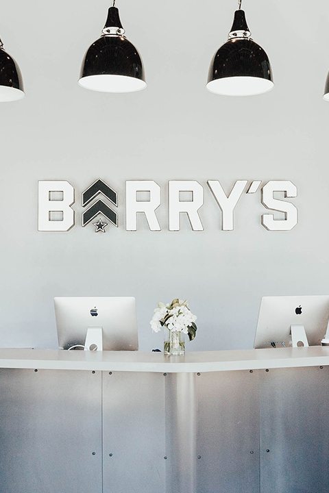 White Barry's Bootcamp sign and grey logo on white wall behind reception desk at San Fransisco studio location