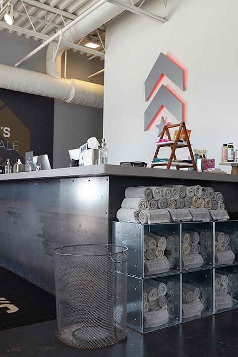 Silver Barry's Bootcamp upward arrows and star logo with red backlighting on wall behind reception desk at Scarsdale studio location