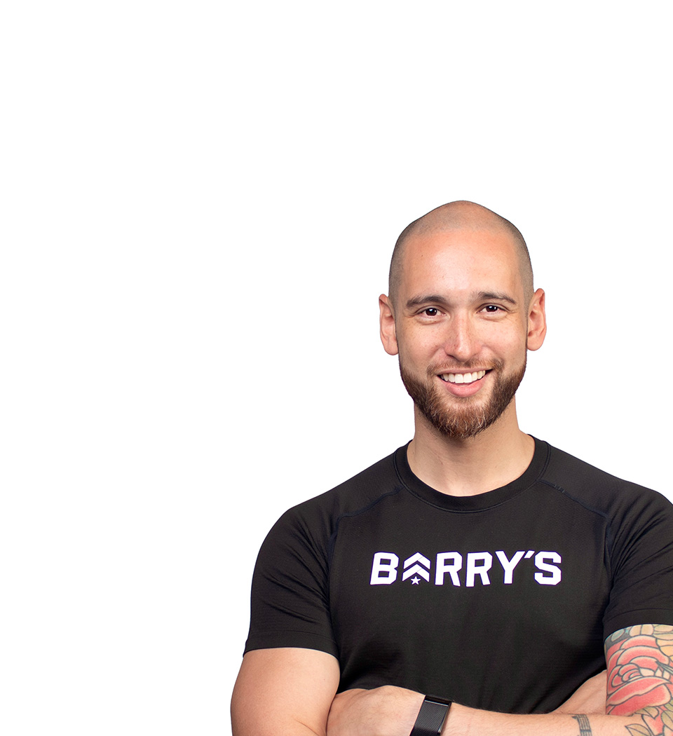 Barry’s instructor wearing a black top standing confidently smiling against a white background