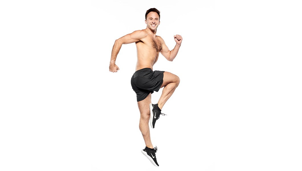 Barry's instructor in a running jump shirtless with black shorts against a white background.