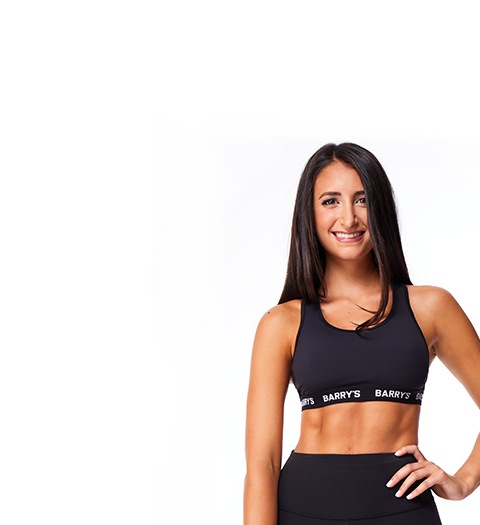 Barry’s instructor wearing a black top standing confidently smiling against a white background