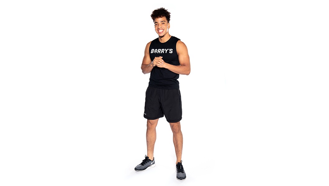 Barry's instructor standing confidently wearing black shorts and tank against a white background