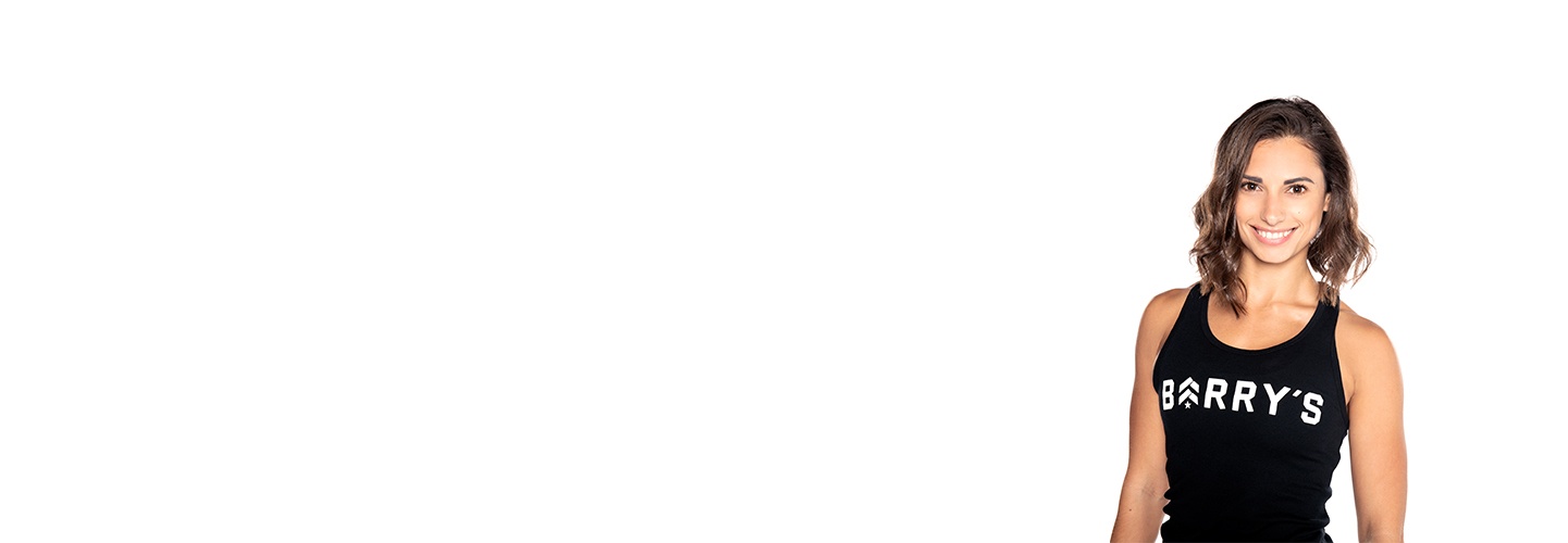 Barry’s instructor wearing a black top standing confidently smiling against a white background