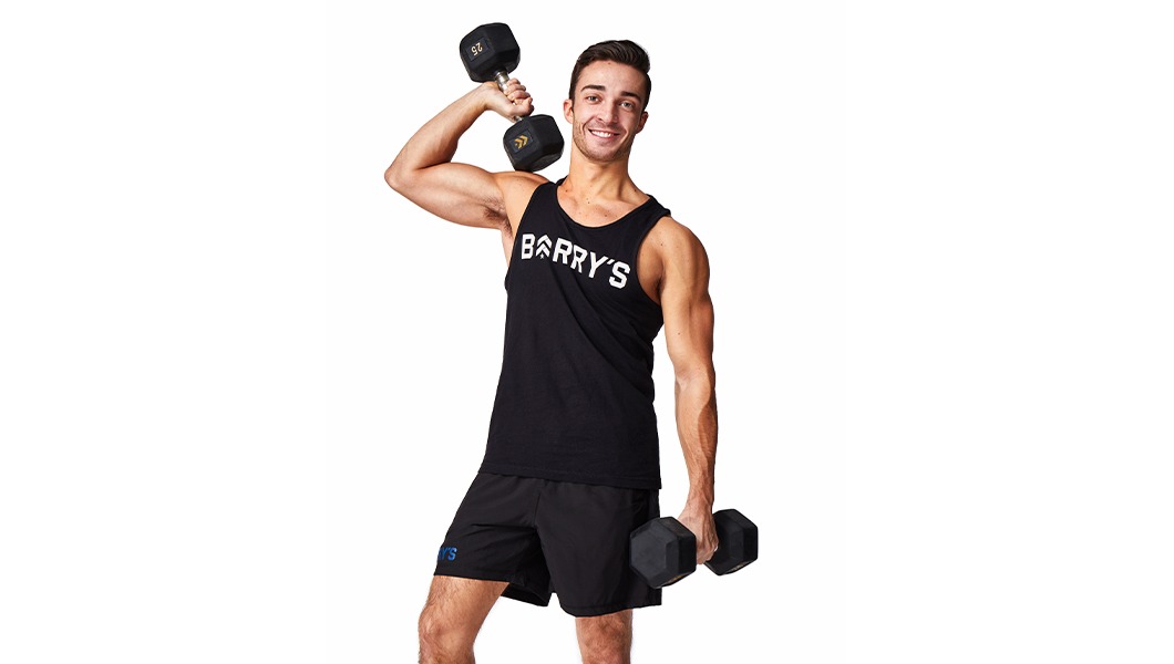 Barry’s instructor wearing a black top standing confidently smiling against a white background holding weights
