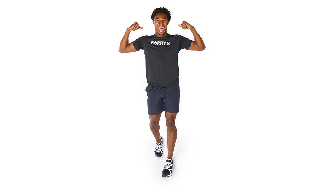 Barry’s instructor wearing a black top standing confidently flexing, smiling against a white background