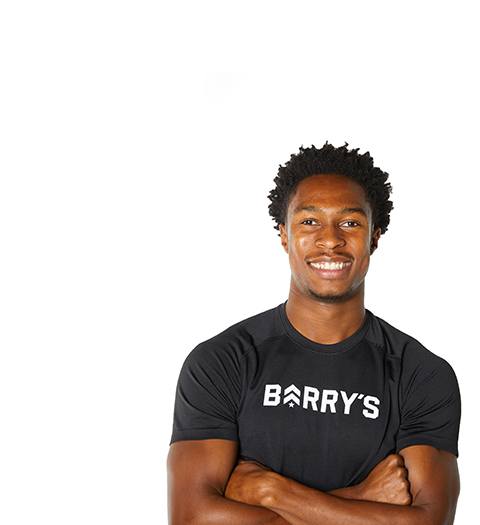 Barry’s instructor wearing a black top standing confidently smiling against a white background