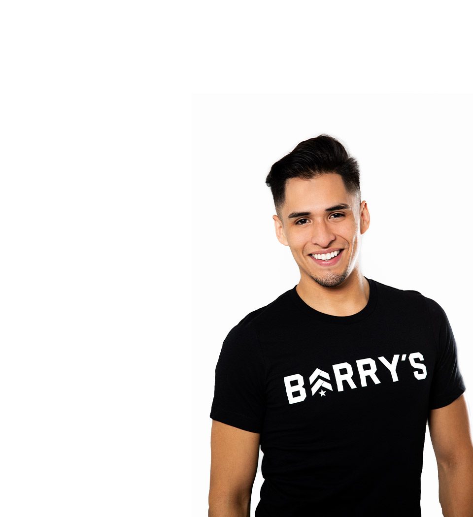 Barry’s instructor wearing a black top standing confidently smiling against a white background