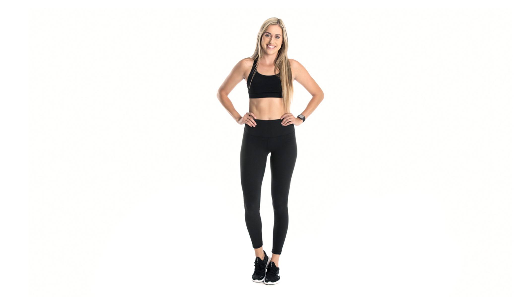 Barry's instructor standing confidently with hands on hips wearing a black top and black leggings against a white background.