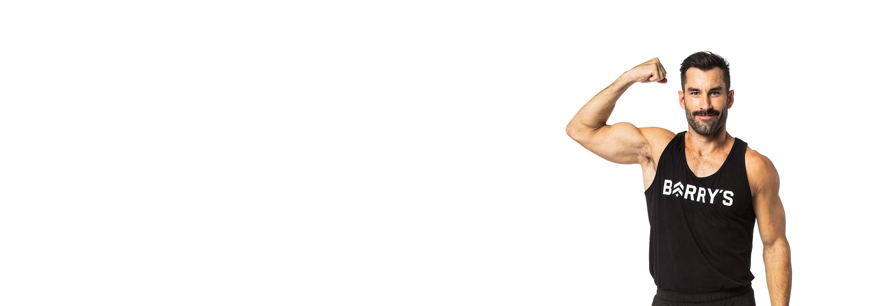 Barry’s instructor wearing a black top flexing his bicep standing confidently smiling against a white background