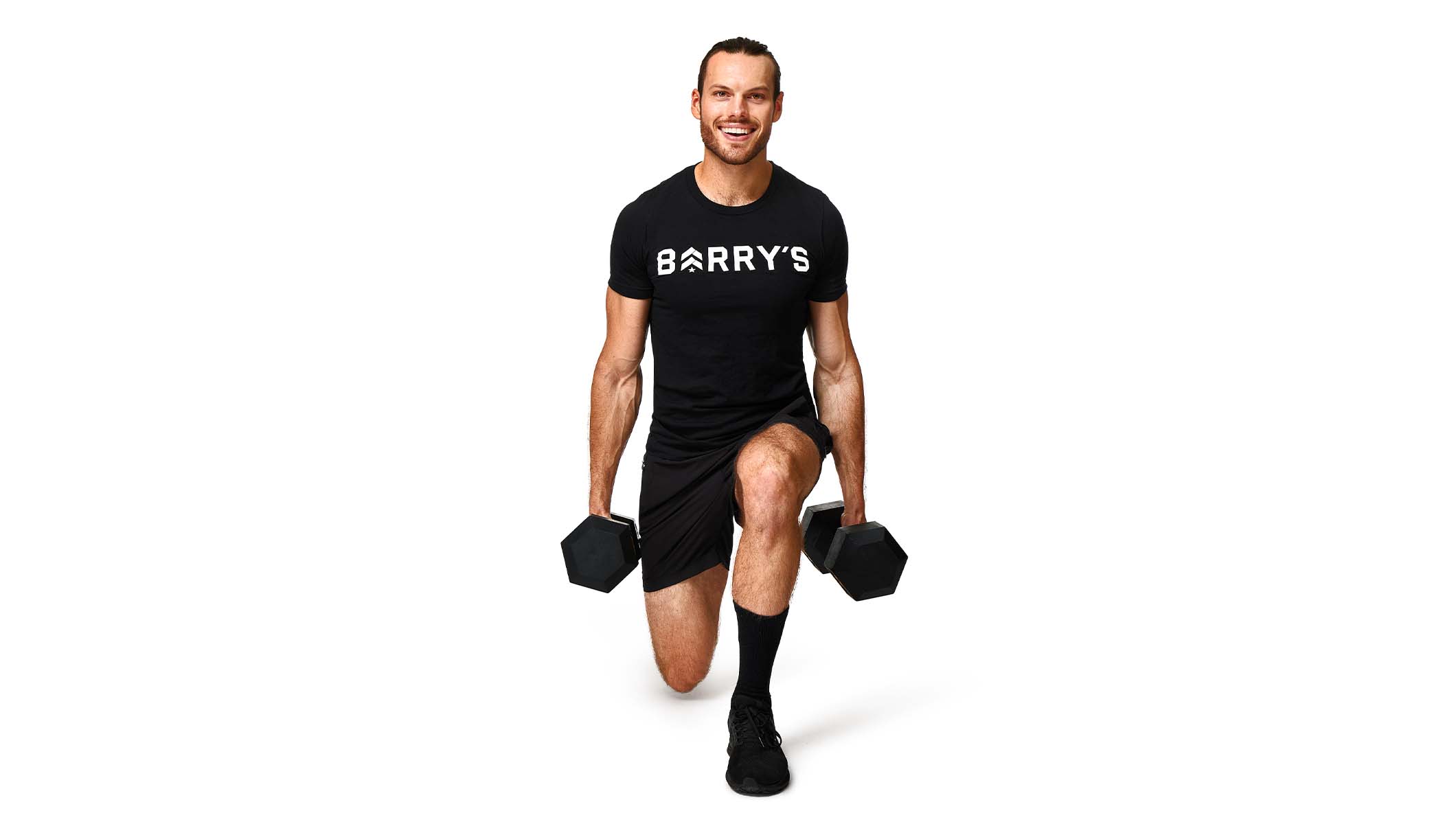 Barry’s instructor wearing a black top standing confidently holding weights smiling against a white background