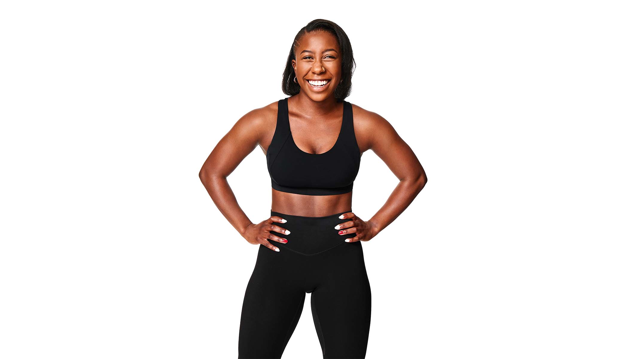 Barry’s instructor wearing a black top standing confidently with hands on hips smiling against a white background