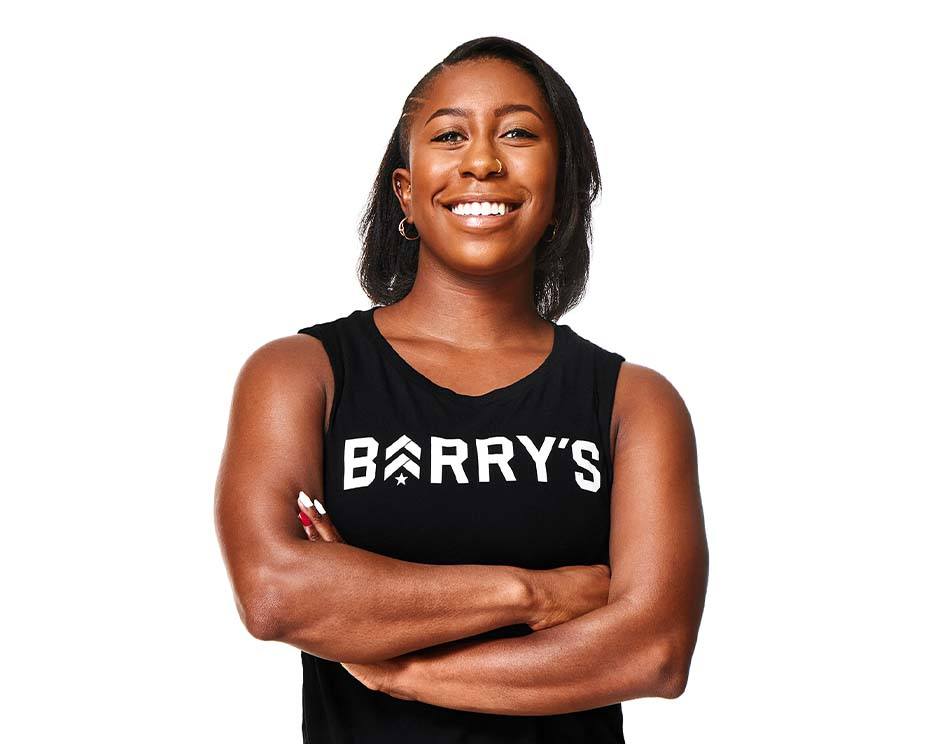 Barry’s instructor wearing a black top standing confidently smiling against a white background