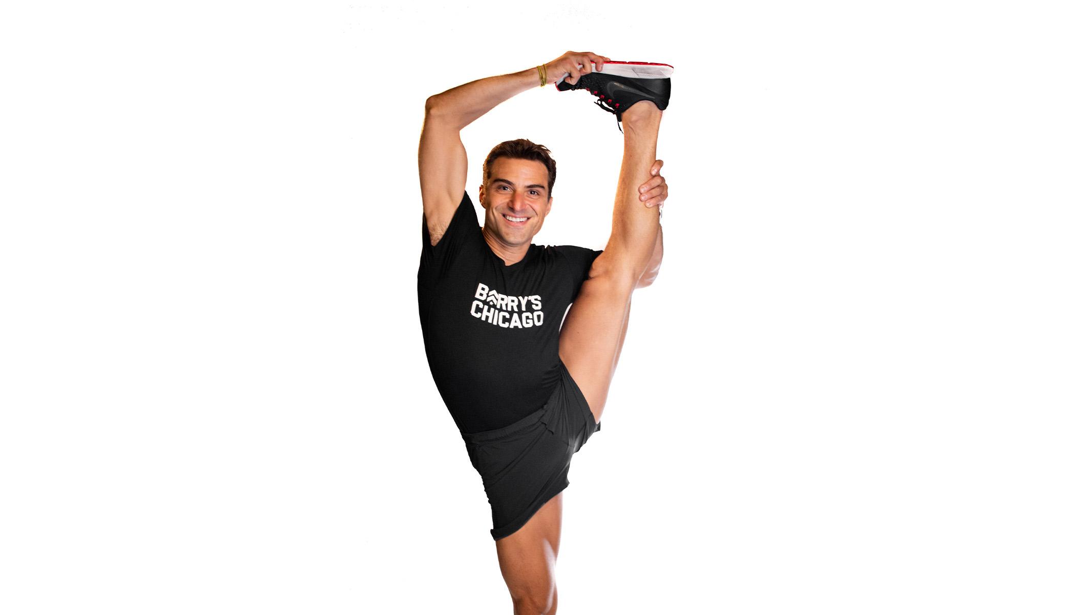 Barry's instructor stretching leg over head wearing a black top against a white background.