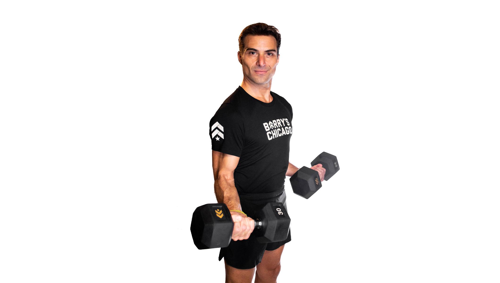 Barry's instructor standing confidently holding weights wearing a black top against a white background.