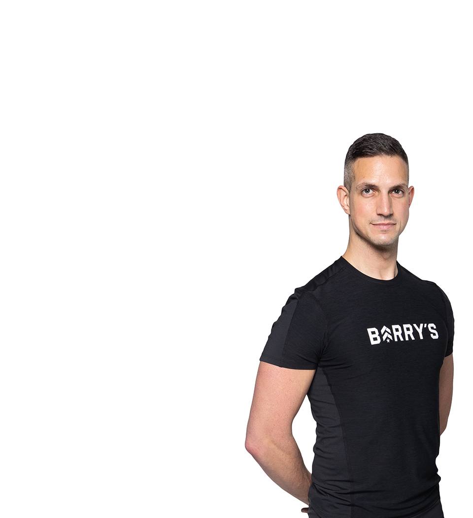 Barry’s instructor wearing a black top standing confidently smiling against a white background