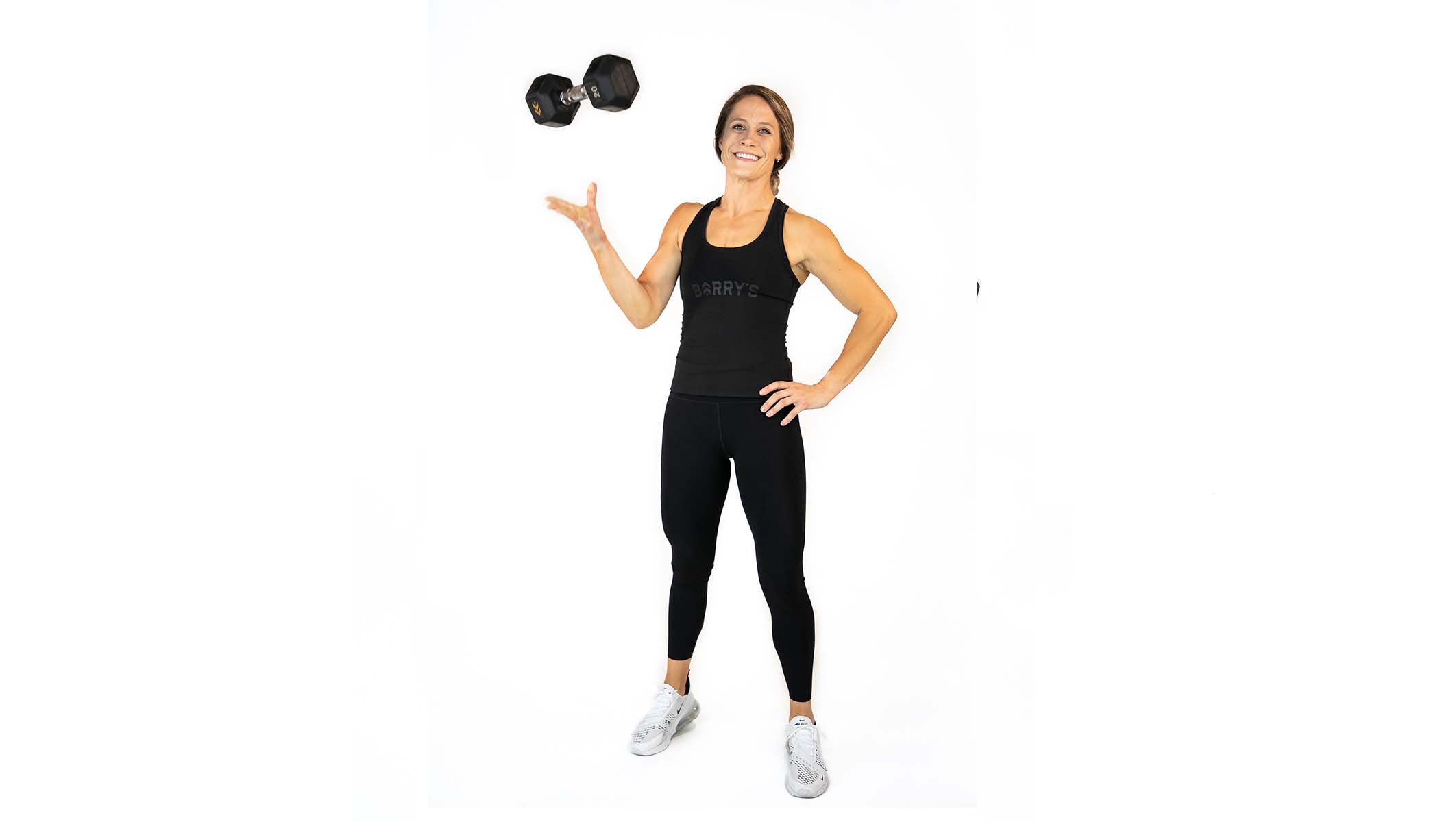 Barry's instructor standing confidently with hands on hips, wearing a black tank top against a white background, ready for the next workout challenge.