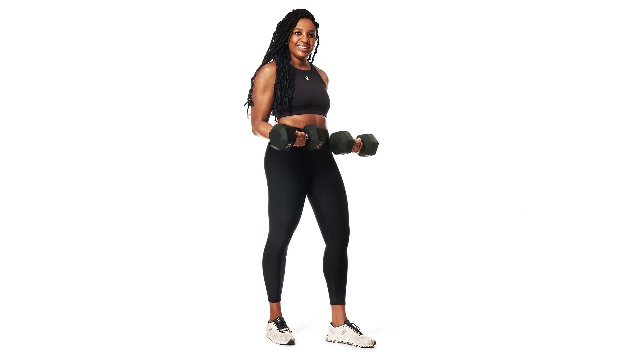 Barry’s instructor wearing a black top standing confidently with weights in hands smiling against a white background