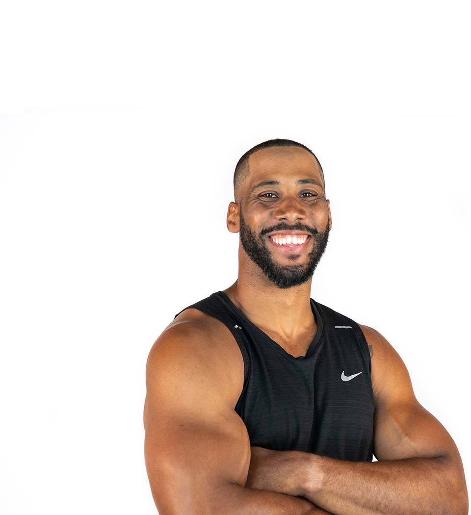 Corey Lemonier instructor standing confidently with arms crossed in front, wearing a black tank top against a white background, ready for the next workout challenge.