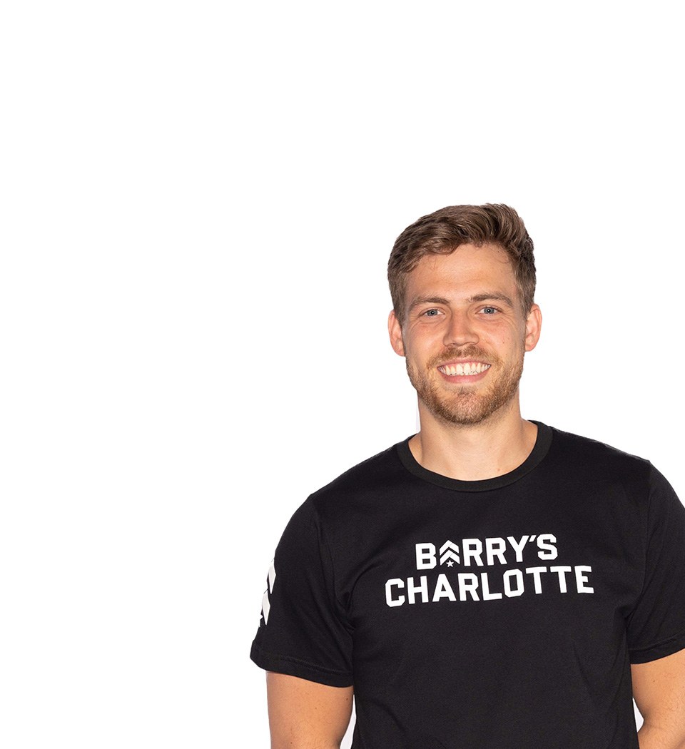 Barry’s instructor wearing a black top standing confidently smiling against a white background