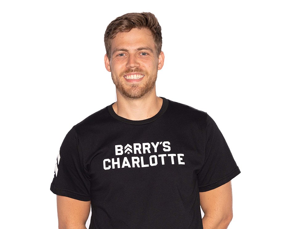 Barry’s instructor wearing a black top standing confidently smiling against a white background