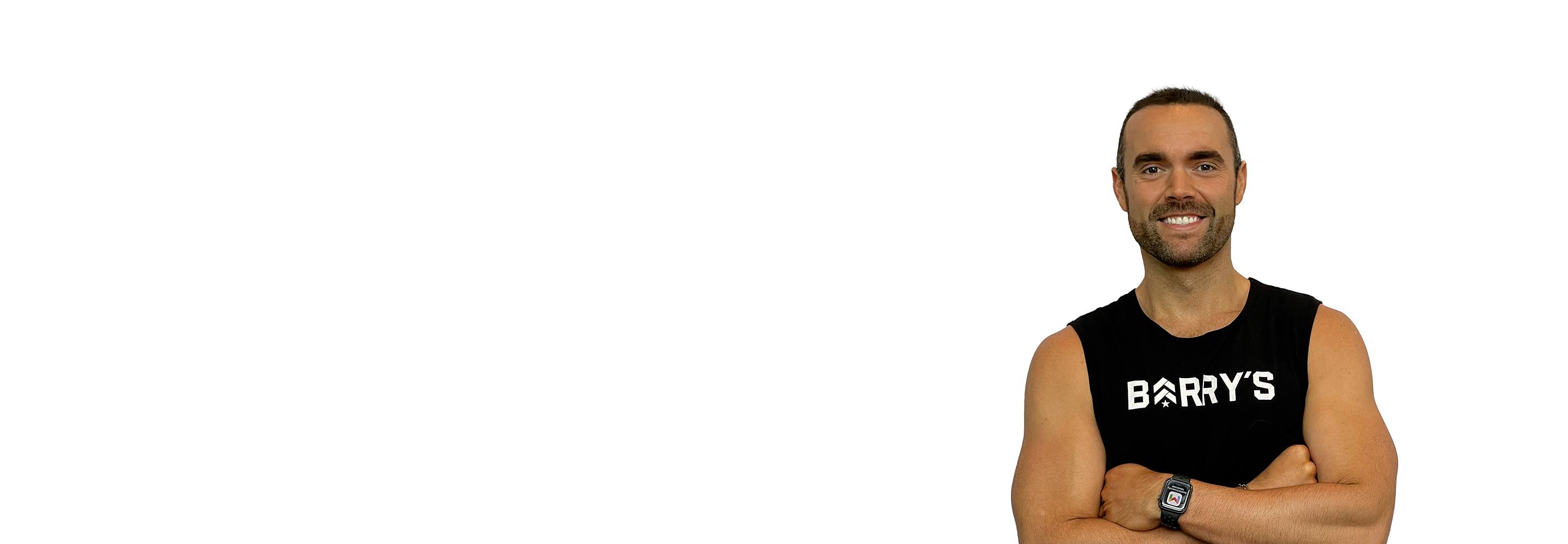 Barry’s instructor wearing a black top standing confidently smiling against a white background
